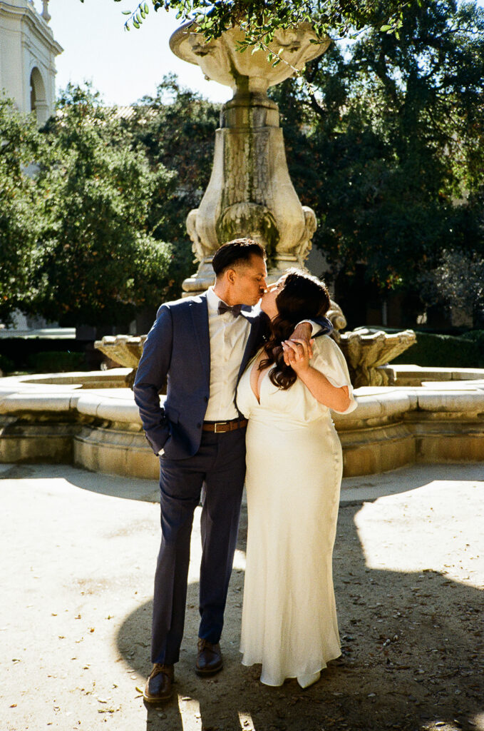 Film photo of a couple kissing in front of the fountain in the courtyard. 