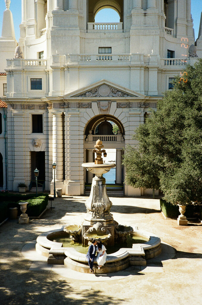 Film photo of a bride and groom sitting at the fountain and kissing.