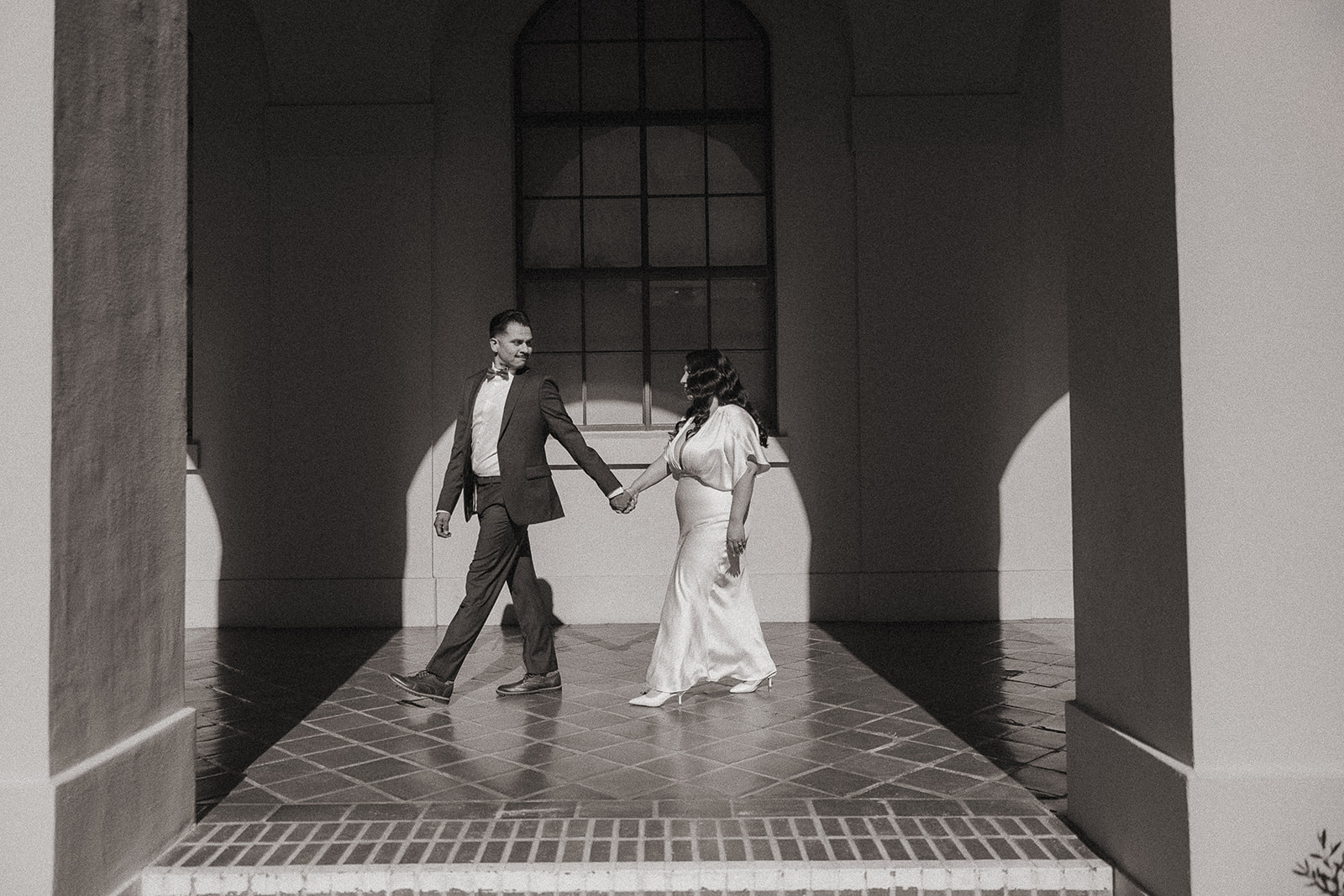 Black and white photo of a bride and groom walking together at the Pasadena City Hall.