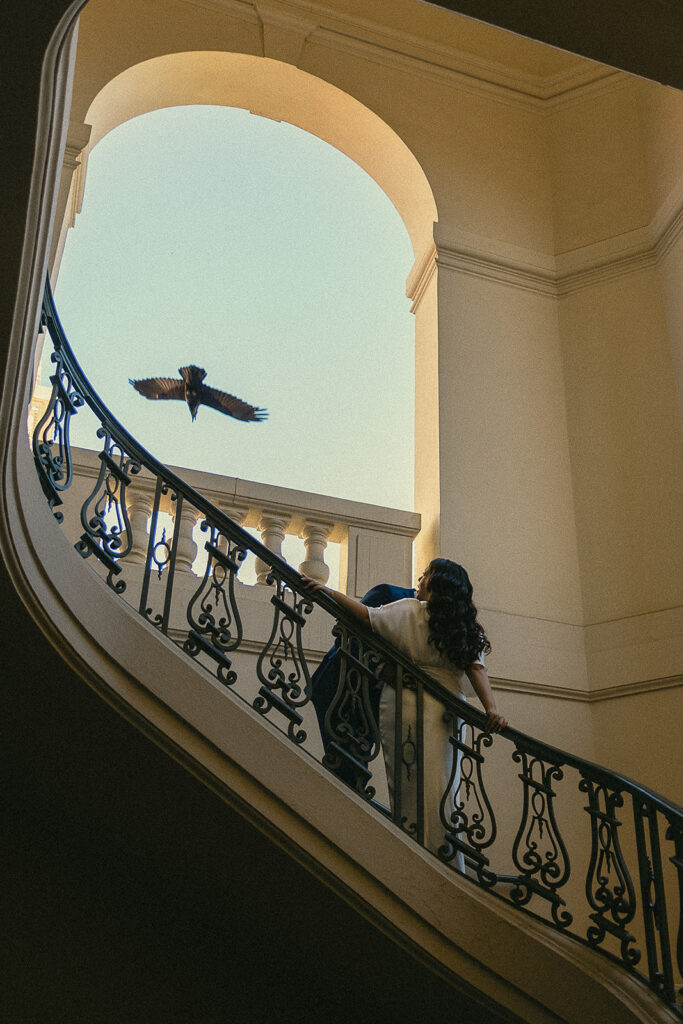 Couple posing on a staircase during their intimate Pasadena City Hall elopement as a bird flies overhead.