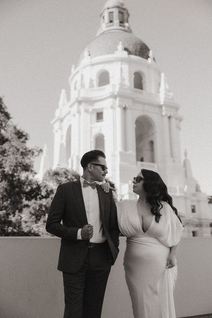 Black and white photo of a couple wearing sunglasses with the Pasadena City Hall rotunda behind them.