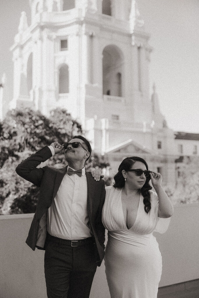Black and white photo of a couple wearing sunglasses with the Pasadena City Hall rotunda behind them.