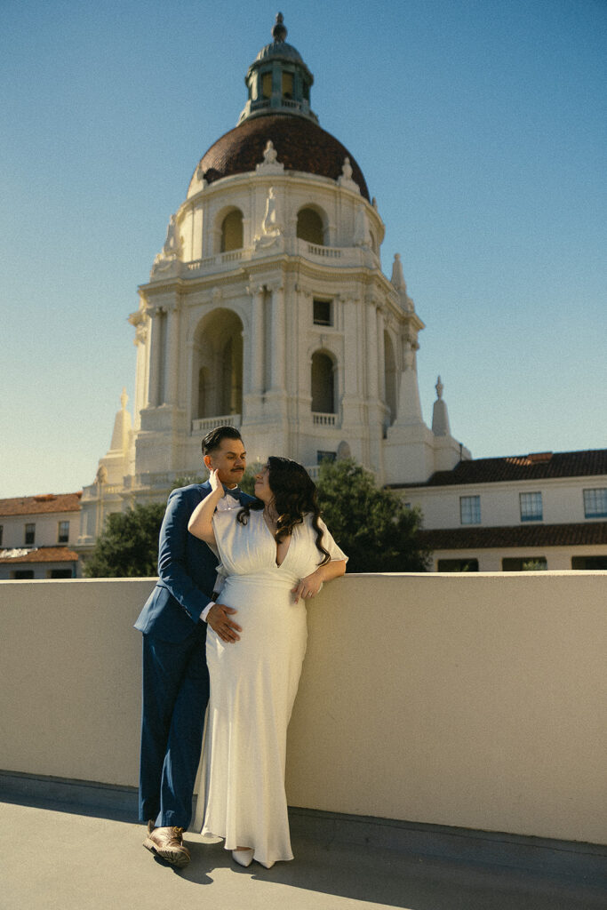 Couple posing against a wall with the rotunda behind them.