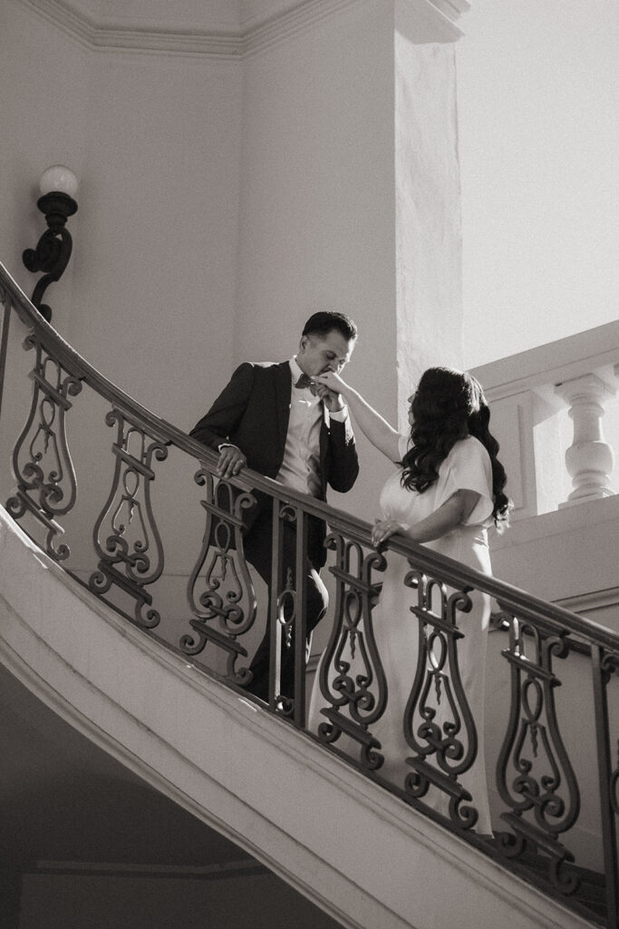 Black and white photo of a man kissing his bride as they ascend the stairs. 