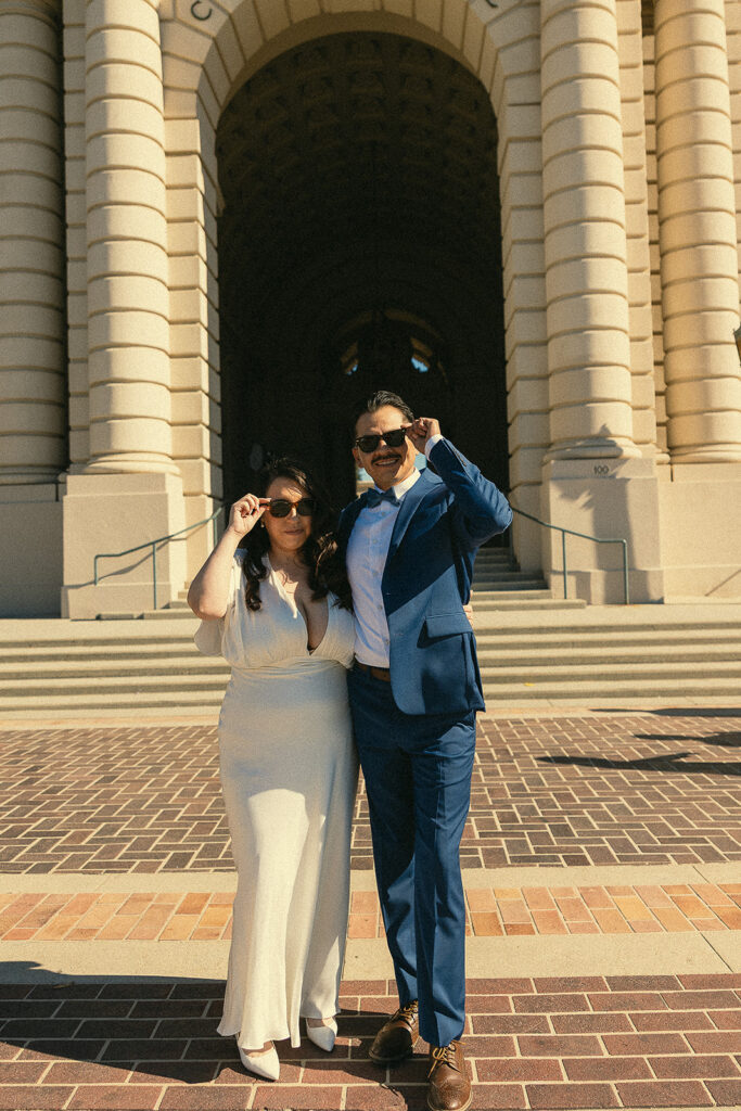 Bride and groom posing in their sunglasses outside of the city hall.