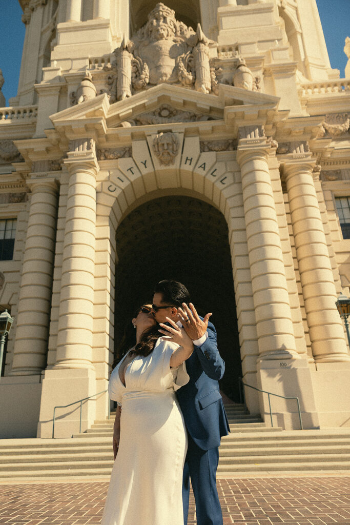 Couple kissing and showing off their wedding rings outside of the city hall. 