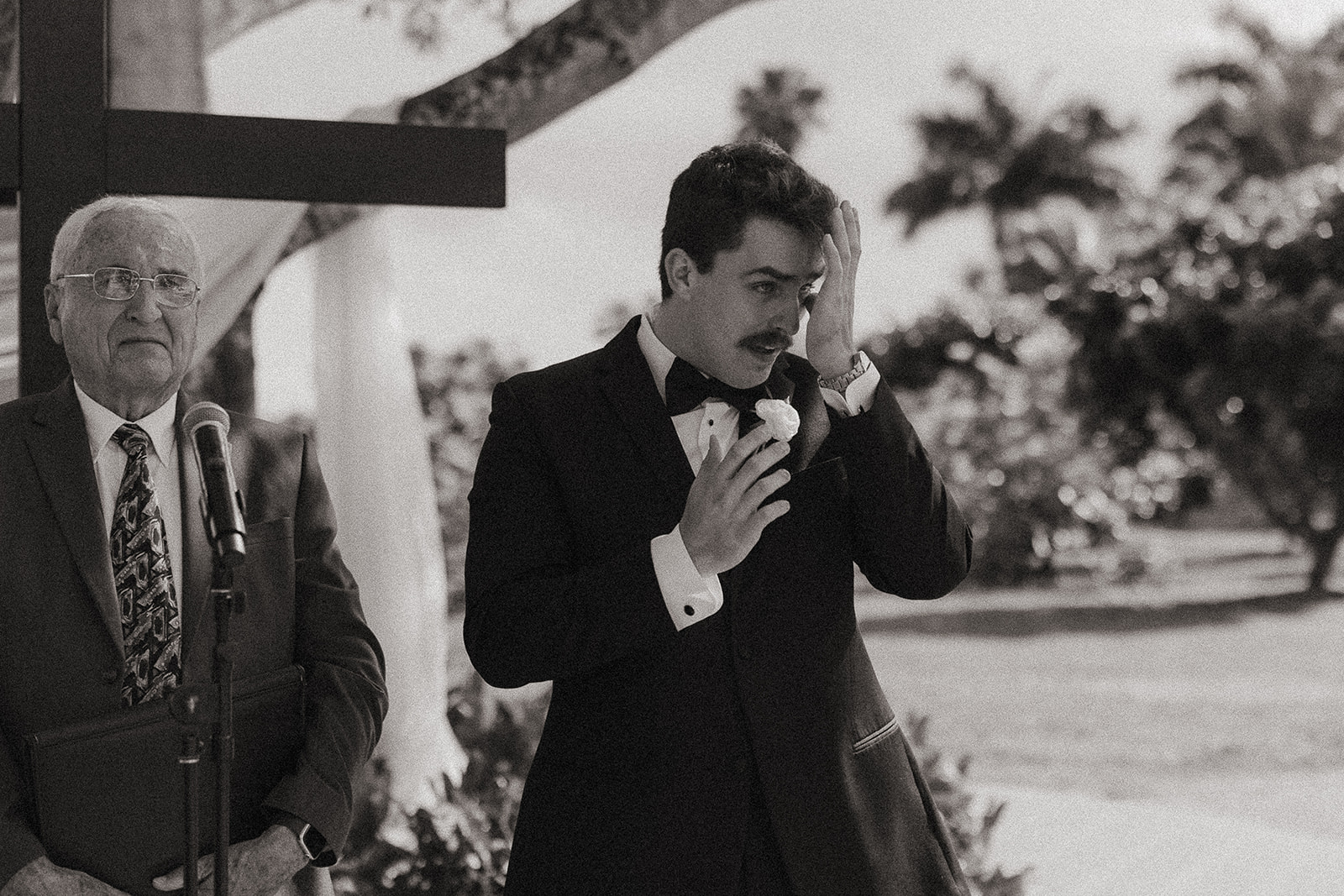 Black and white photo of the groom getting emotional as he sees his bride being walked down the aisle.