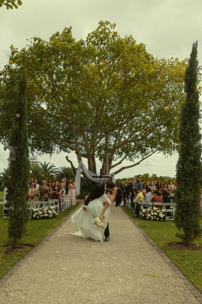 Bride and grooms end of aisle dip kiss after their Cinco Farm Gardens Miami wedding ceremony.