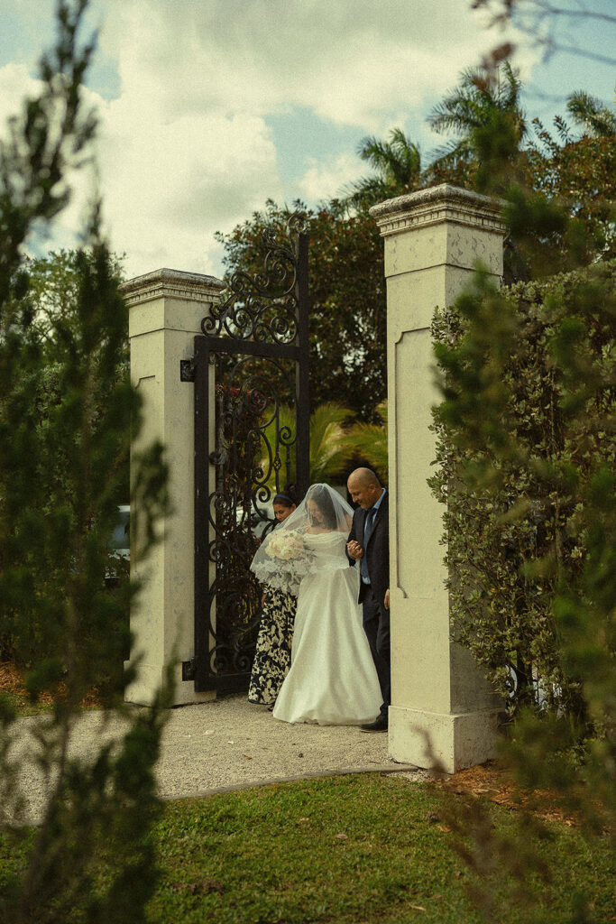 Bride being walked into the ceremony by her mother and father for her Cinco Farm Gardens Miami wedding ceremony.