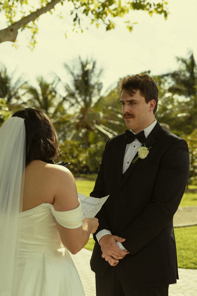 Groom listening as the bride reads her vows to him during their Cinco Farm Gardens Miami wedding ceremony.