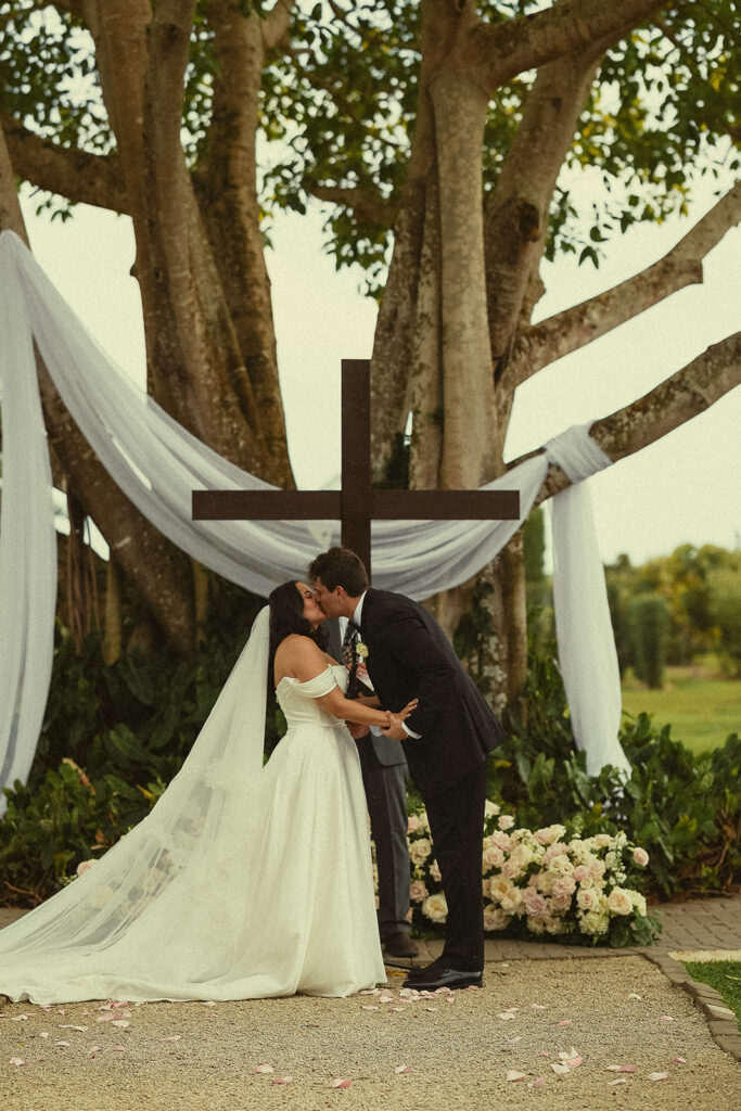 Bride and groom kissing in front of a cross altar. 