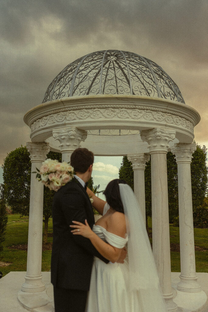 Bride and groom posing in front of white gazebo