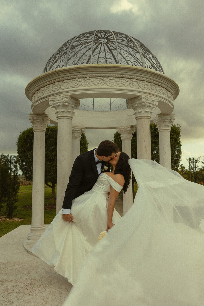Bride and groom kissing in front of white gazebo.