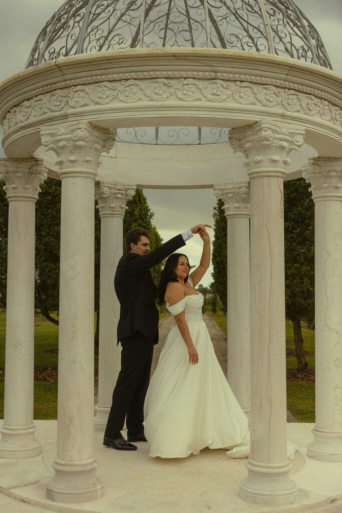 Bride and groom twirling inside of a white gazebo.