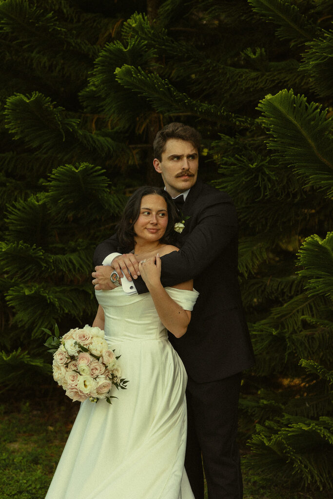 Bride and groom posing with the backdrop of tropical tree leaves.