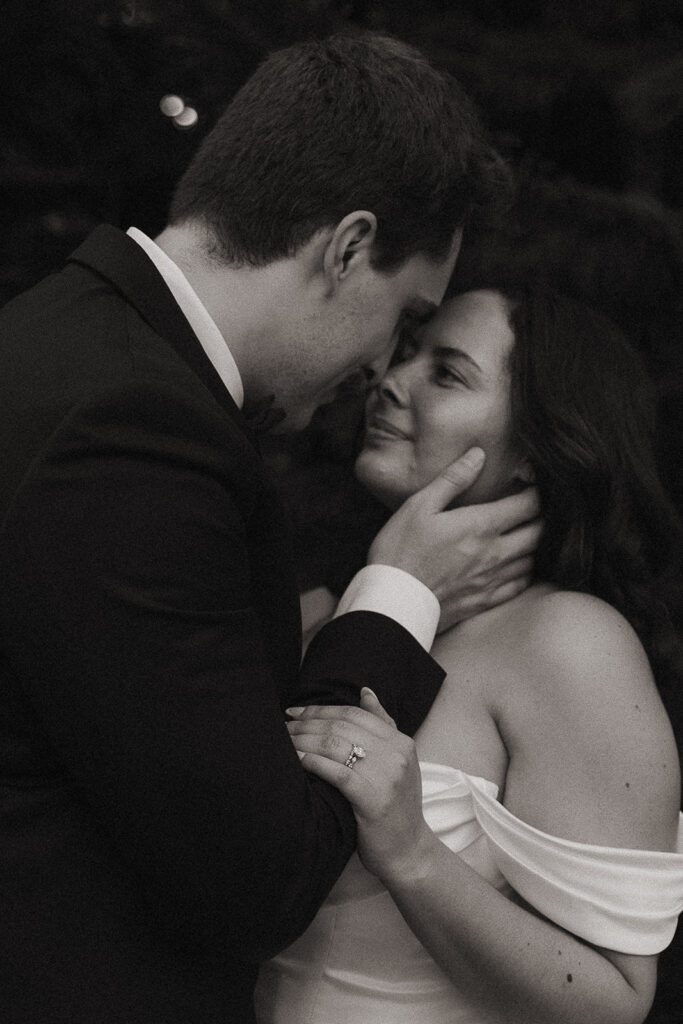 Black and white close up portrait of the groom touching the brides cheek lovingly. 