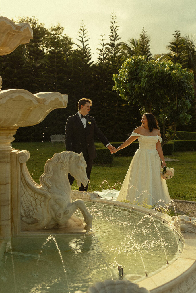 Bride and groom holding hands and walking around the water fountain at Cinco Farm Gardens in Miami, Florida.