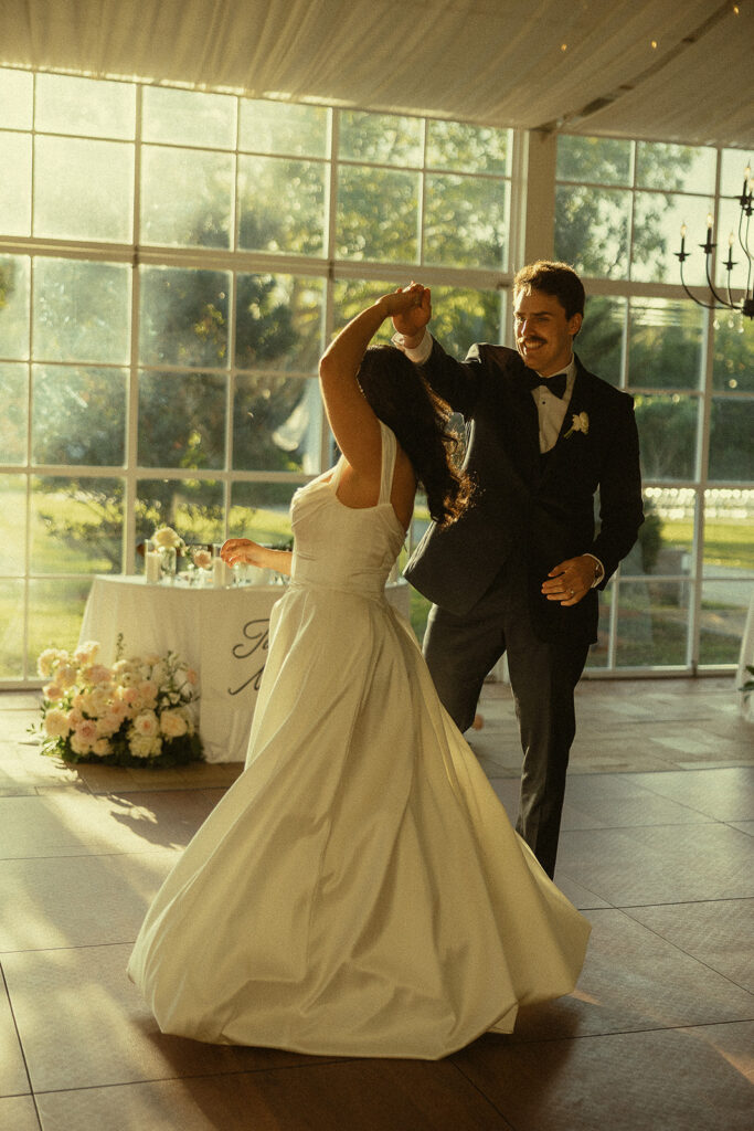 Bride and groom twirling during their first dance in the glass pavilion.