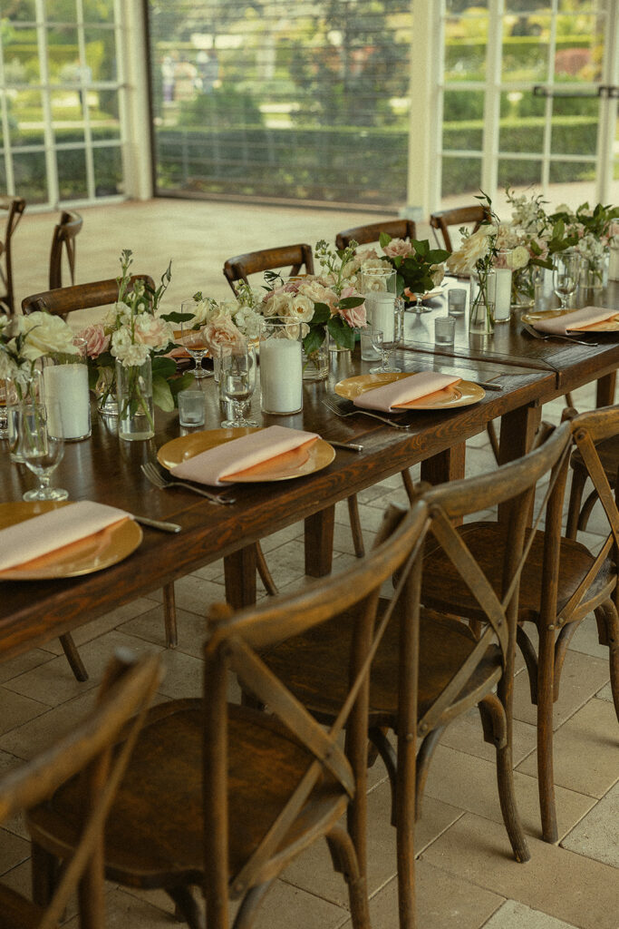 Long wooden reception tables with gold chargers, florals, and candles for a Cinco Farm Gardens wedding reception in Miami, Florida.