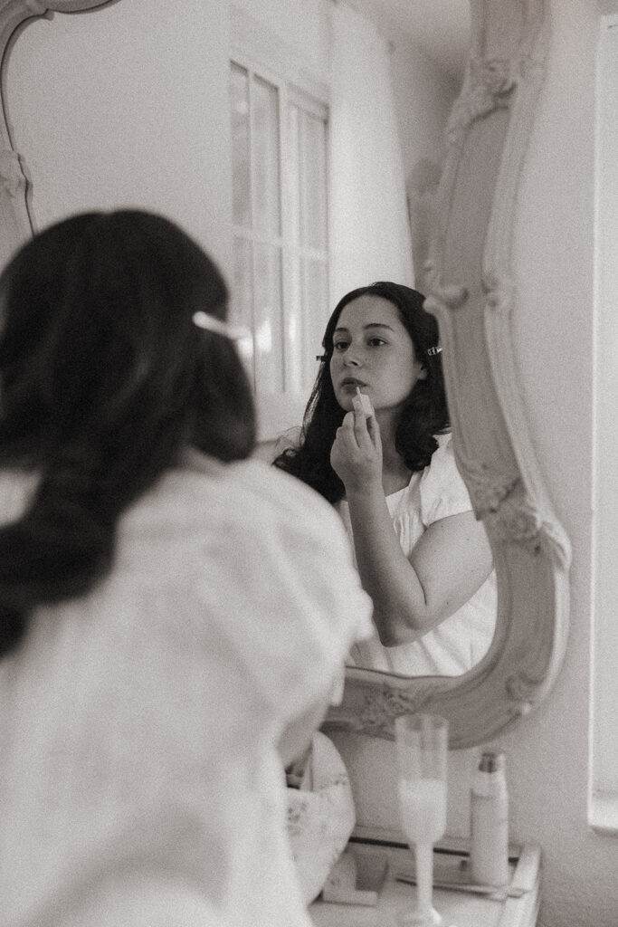 Bride applying lipstick in the mirror before her wedding.