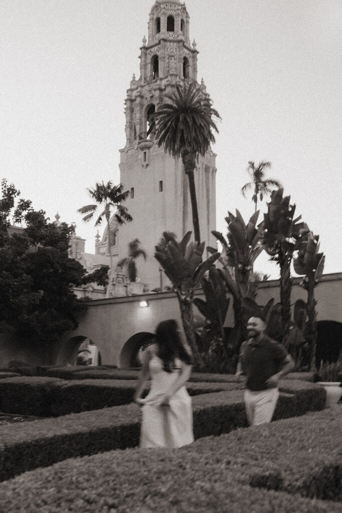 Black and white engagement photo of couple walking through Alcazar Garden at Balboa Park.
