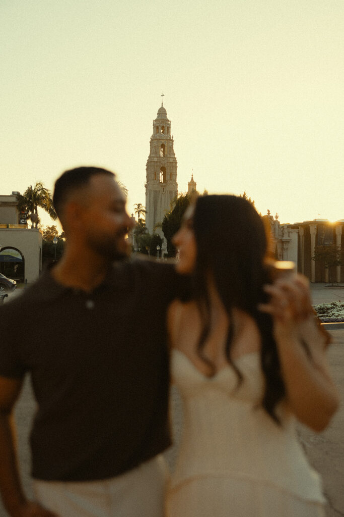 Couple laughing with the California Tower in the background during Balboa Park engagement photos.