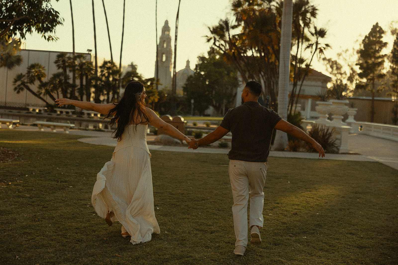 Couple holding hands and running in Balboa Park for their San Diego engagement photos.