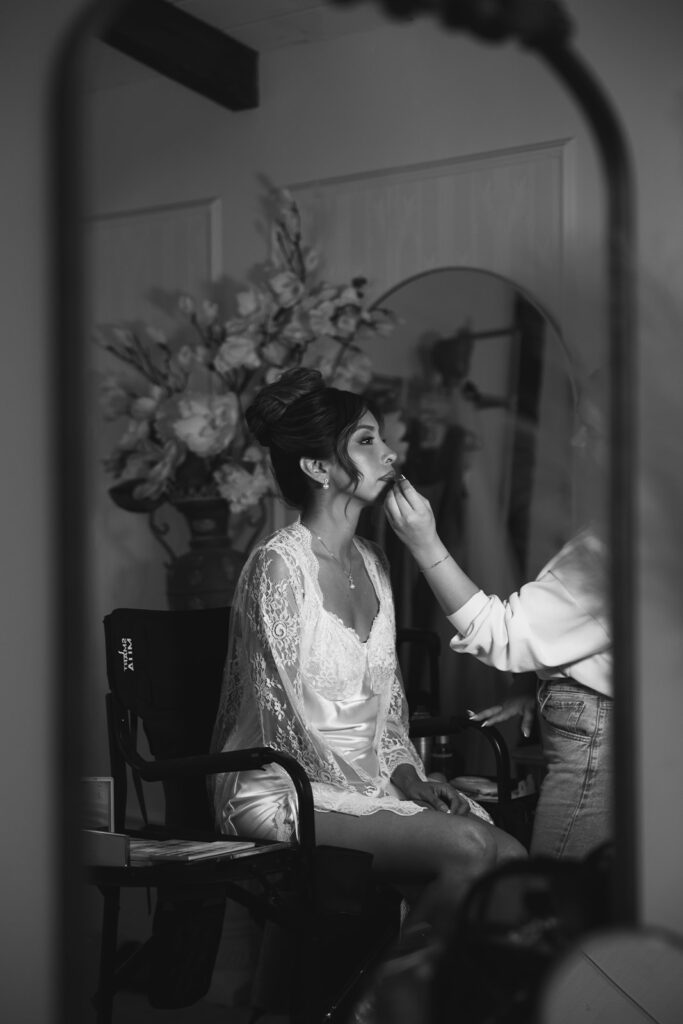 Black and white photo of a bride getting her makeup done in the bridal suite at Jeune Perché.
