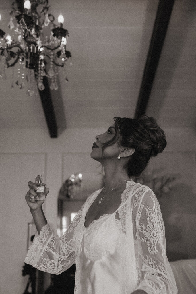 Black and white photo of a bride spraying perfume on herself in the bridal suite.