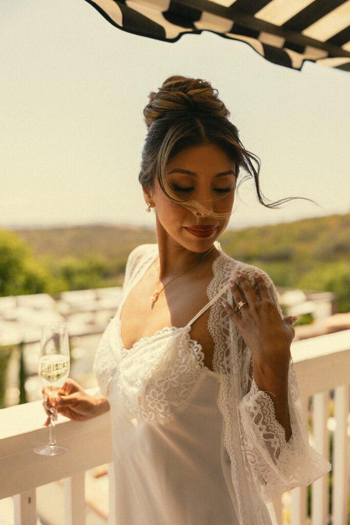 Bride posing with a glass of champagne on the balcony of the bridal suite at Jeune Perché. 