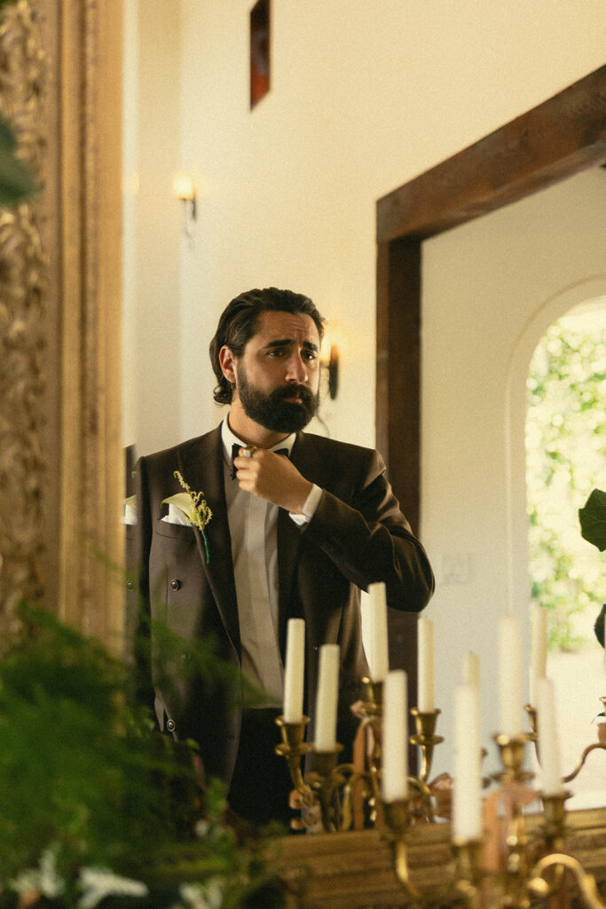 Groom adjusting his bowtie in the mirror inside the grooms suite.