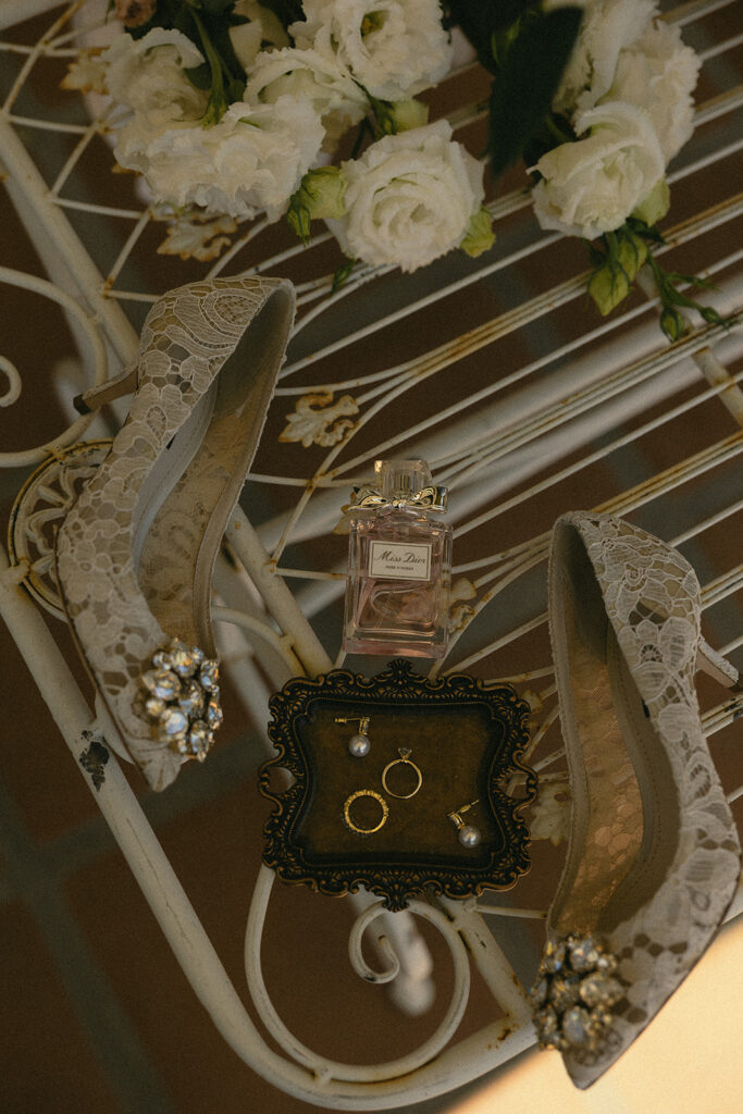 Brides wedding details with heels, perfume, rings, and florals.