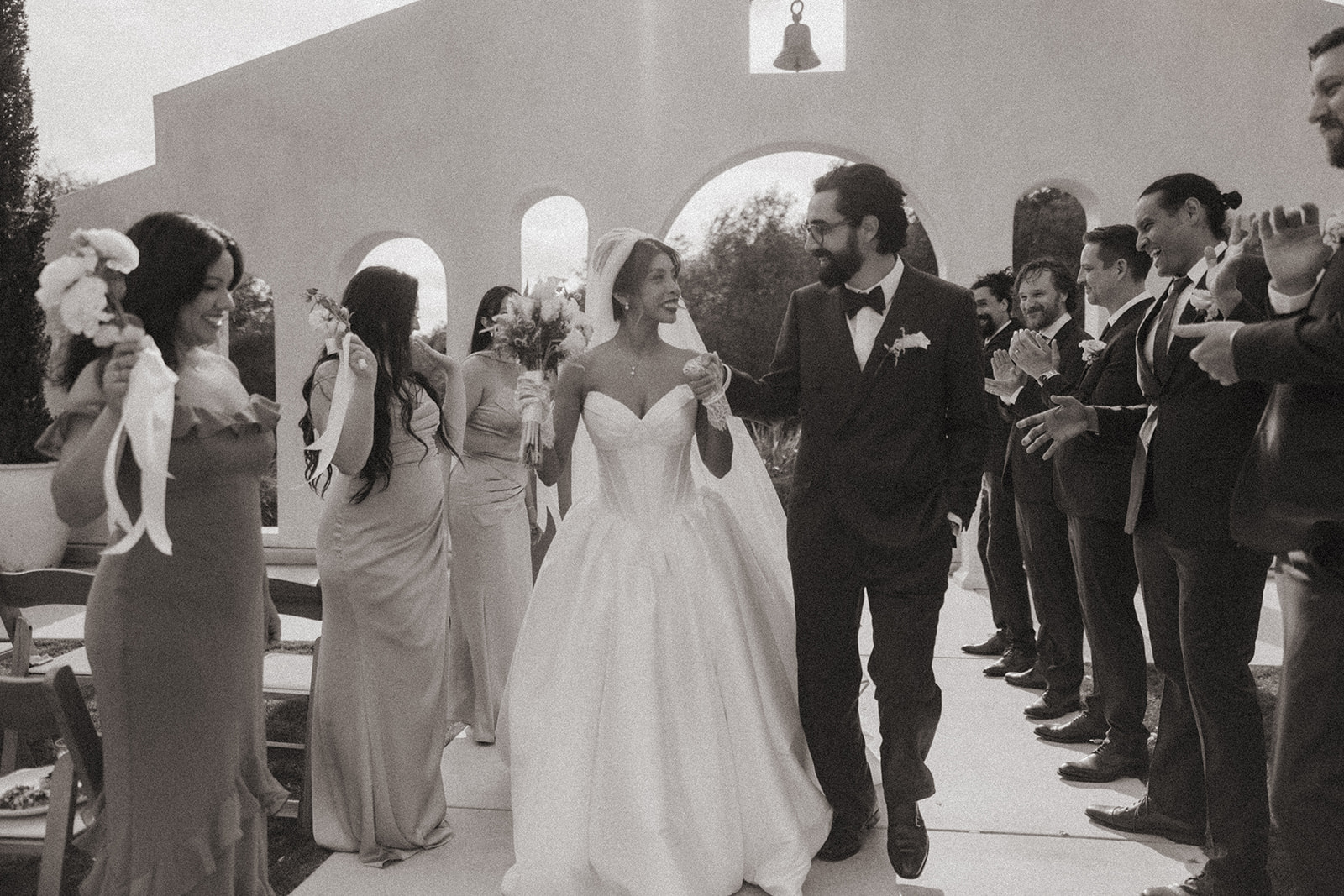 Black and white wedding party photo of a bride and groom walking back down the aisle as husband and wife.